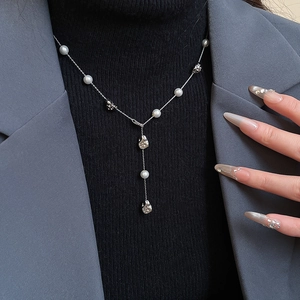Detail of a silver Y-shaped pearl necklace on a black knit and grey blazer background