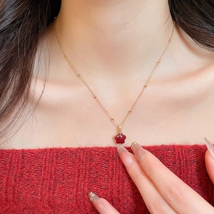 Close-up of gold chain necklace with red star pendant on neck with red knitwear