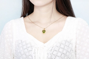 Detail of gold heart pendant necklace with green birthstone worn by a model