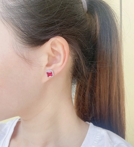 Close-up of a square red ruby stud earring with a diamond halo on a model's ear