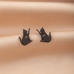 Close-up of black cat stud earrings with heart cut-out on beige silk fabric