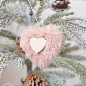 Pink plush heart Christmas tree ornament with wooden accent hanging on a snowy branch