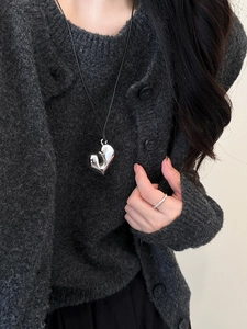 Primo piano di una collana con ciondolo a cuore lucido e cordino nero su un maglione grigio