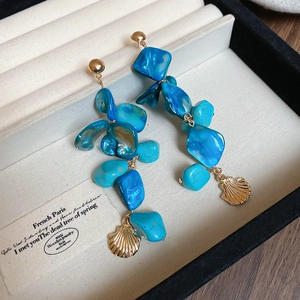 Macro detail of gold-plated shell earrings with blue stones on a beige jewelry display