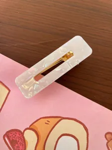 Detail of pearlescent white acrylic hair clip with golden metal clip on wood surface