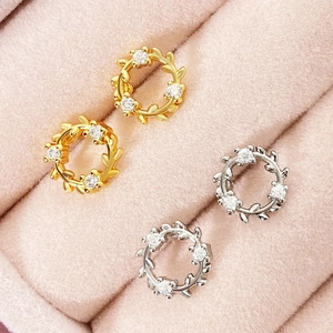Leaf wreath stud earrings with cubic zirconia in gold and silver on pink velvet