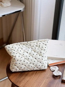 Detail of white quilted heart pattern makeup bag on a wooden table with home decor