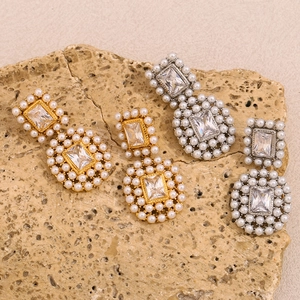 Detailed view of 18K gold and silver earrings with rectangle zircons and pearls on rock