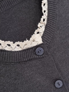 Détail d'un pull en tricot gris foncé avec col en dentelle blanche et boutons foncés
