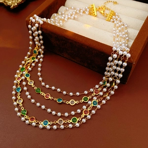 Detail of multilayer necklace featuring white pearls and colorful gemstones on gold base