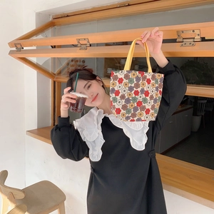 Floral canvas handbag with yellow handles held by a model in a cozy cafe setting