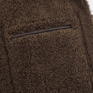 Detail of dark brown faux shearling fabric with a welt pocket and trim on the jacket