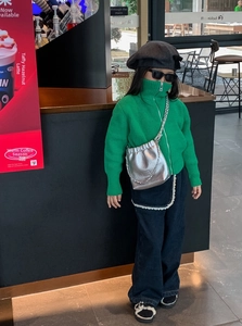 Mädchen mit grüner Strickjacke und silberner Falten-Kettentasche in einem Café