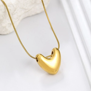 Polished golden heart pendant necklace with fine snake chain on white marble base