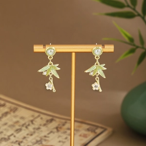 Detail of green bamboo leaf earrings with white plum blossom and tassel on a gold stand