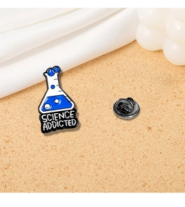 Macro shot of Science Addicted enamel pin with blue chemical flask on sand surface