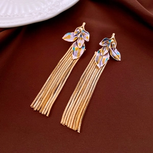 Macro detail of leaf-shaped earrings with purple enamel and long golden snake chain tassels