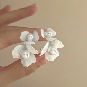 Minimalist C-shaped white floral earrings with pearls held in hand for a natural look