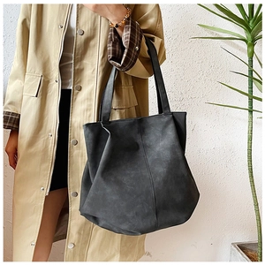 Detailed view of large black tote bag with shoulder straps worn over a beige trench coat