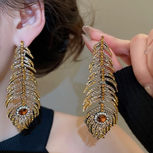 Close-up of luxury feather drop earrings with amber and white rhinestones on silver needle