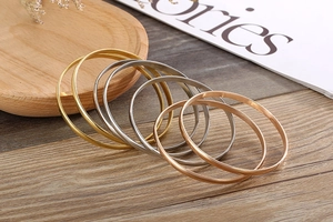 Three-color minimalist titanium steel bangles stacked on a rustic wooden textured surface