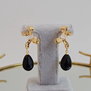 Golden bow earrings with zircon inlay and black teardrop pendants on grey velvet stand