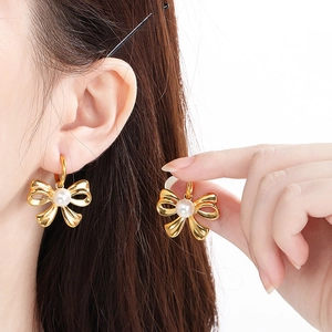 Detail of elegant gold bow earrings with white pearls shown on a female model