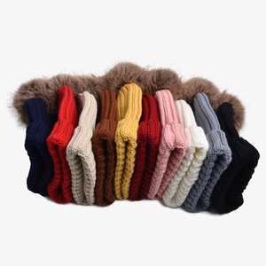 Detailed stack of multi-colored knitted beanies with fluffy brown faux fur pom-poms