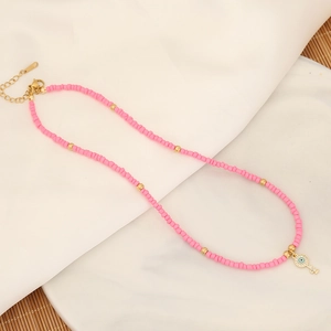 Bohemian pink bead necklace featuring a gold Evil Eye key pendant on a white ceramic plate