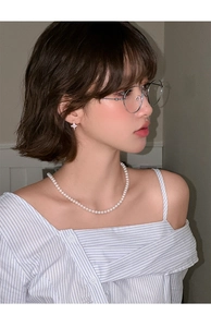 Detail view of pearl necklace and star stud earrings worn with a light blue striped shirt
