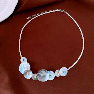 Detailed shot of white beaded necklace with iridescent shell pendants and metal clasp