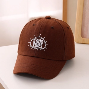Dettaglio del ricamo bianco 'GOOD VIBES' su un cappellino da baseball marrone