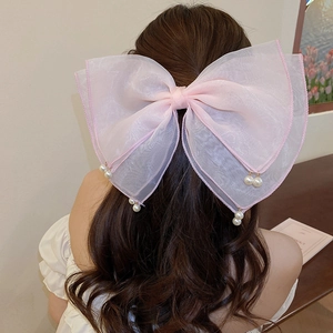 Close-up of pink organza bow hair clip with pearl tassels on wavy dark hair