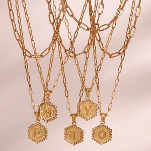 Macro detail of gold hexagonal initial pendants on elegant paperclip link chains