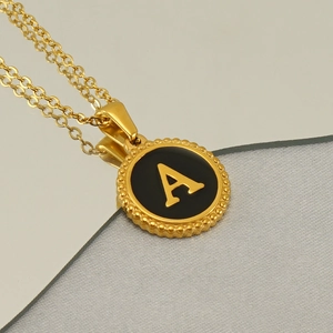 Close-up of 18K gold letter A pendant with black enamel and vintage beaded edge design