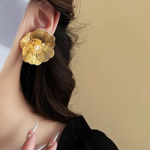 Detail of gold hollow flower earring with brushed finish and rhinestone center