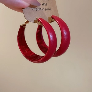 Detail view of large red leather wrapped hoop earring with gold-tone metal clasp