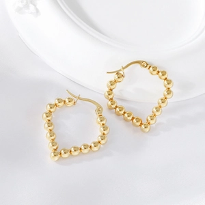 Elegant gold beaded heart-shaped earrings on soft white silk and ceramic backdrop
