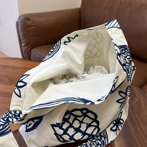 Détail d'un sac cabas en toile beige avec imprimé d'ananas bleu sur un canapé marron