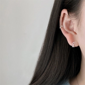 Close-up of a silver cross ear cuff and infinity stud earring set worn by a model