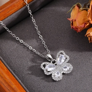 Detail of silver bow pendant with white zircons on textured grey fabric with a rose