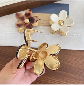 Detail view of flower-shaped hair claws in tortoiseshell and cream resin with metal spring