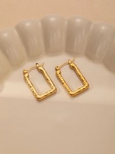 Detailed close-up of golden rectangular earrings with a vintage hammered texture surface