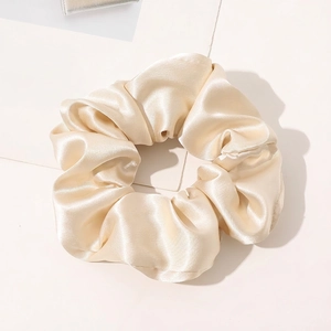 Macro shot of off-white silk scrunchie showing glossy satin texture and elegant folds