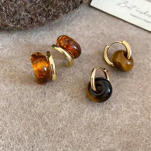 Vintage gold hoop earrings with amber tiger eye resin beads on a cozy textured background