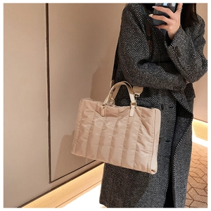 Beige quilted nylon tote bag featuring leather handles and golden hardware shown on a model
