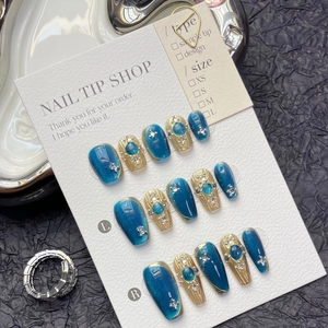 Detail of blue cat-eye and gold embossed press-on nails with rhinestone accents
