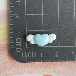 Mini light blue resin heart with white wings accessory on a measuring scale mat