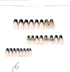 Macro detail of long coffin press-on nails with black French tips and gold bee charms