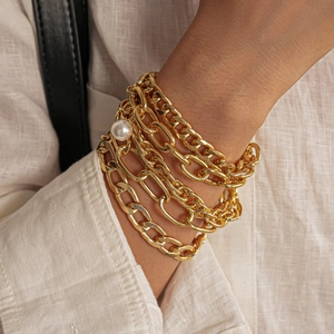 Detail of layered gold metal chains with a round white pearl on white linen fabric